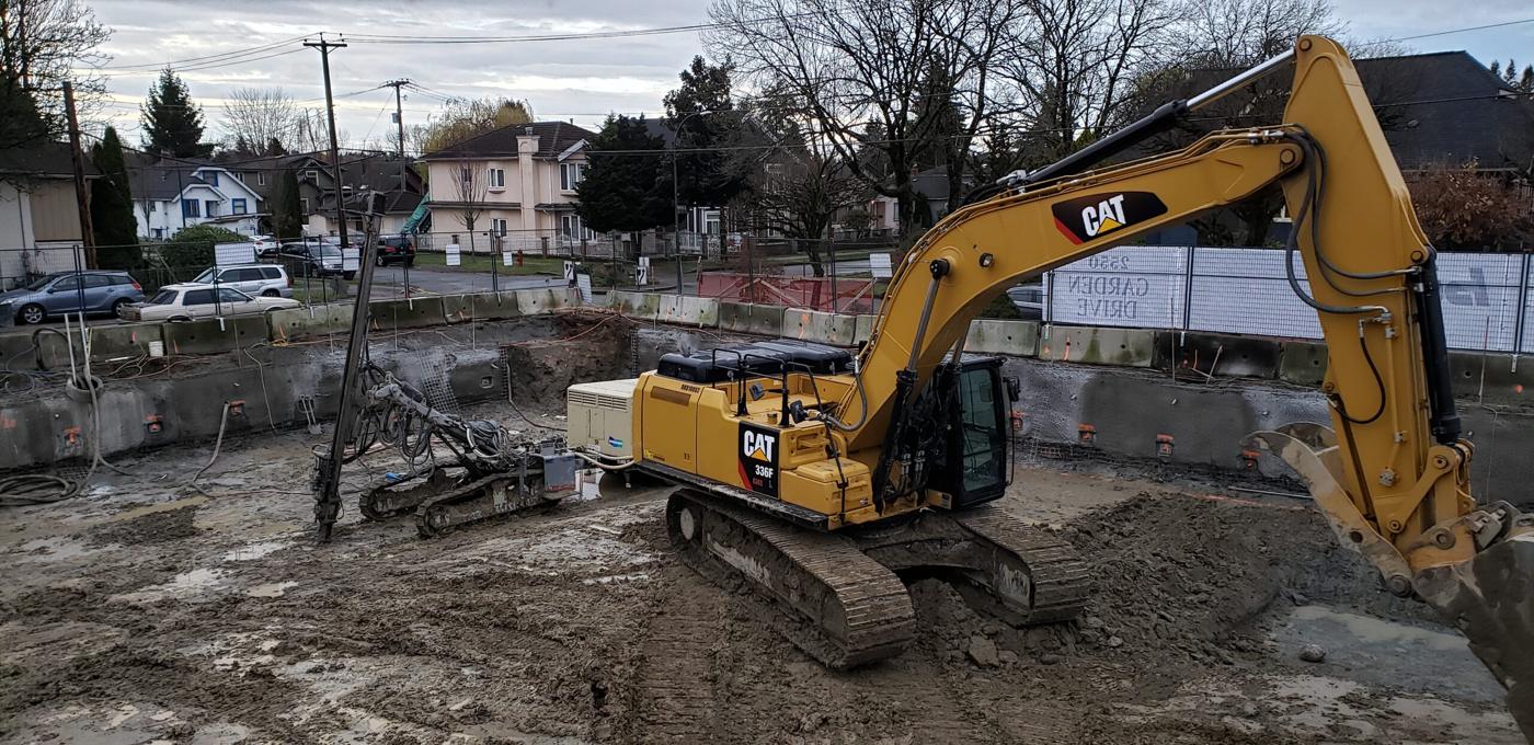 Excavator and drill rig working inside a shored excavation